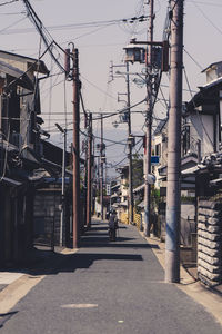 Rear view of person walking on road amidst buildings in city