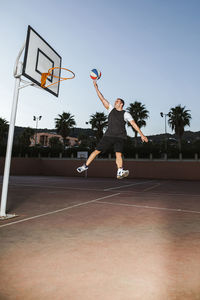 Basketball player in black and white sport clothes jumping and making dunk while training on sports ground