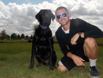 Portrait of young man with black labrador on grassy field