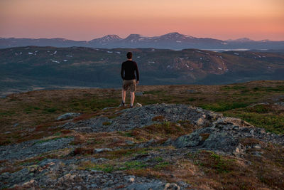 Rear view of man standing on mountain against sky