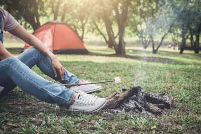 Low section of man heating marshmallow on campfire in forest