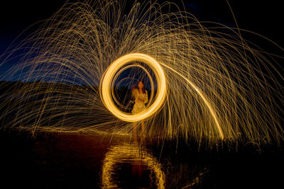 Burning steel wool spinning, trajectories of burning sparks on the surface of water lake by women