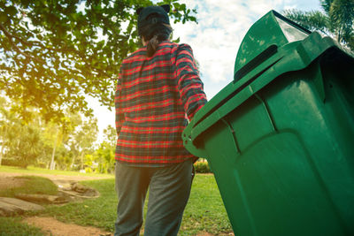 Rear view of woman holding garbage can against sky