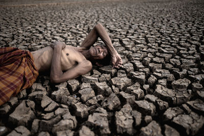 High angle view of shirtless man sleeping on drought land
