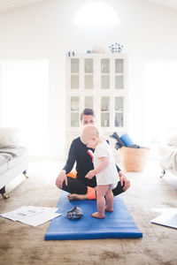 Working mother practicing yoga while daughter standing on exercise mat at home