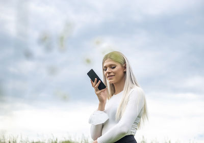 Young woman using mobile phone against sky