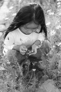 Girl holding spinner while crouching by plants at field