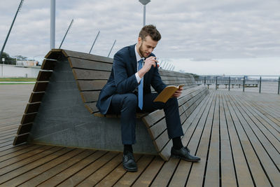 Young businessman reading book while sitting on bench