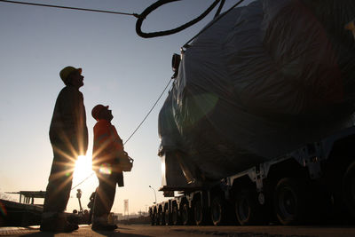 Close-up of two worker beside a heavy truckload in a harbor. 