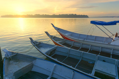 Empty boats moored in sea against sky during sunset