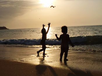 Silhouette friends on beach against sky during sunset