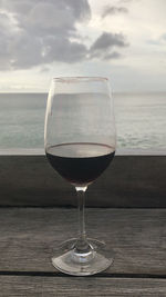 Wineglass on table by sea against sky