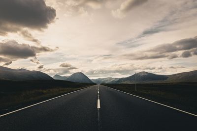 Empty road leading towards mountains against sky