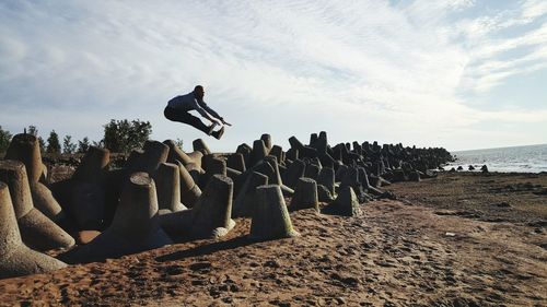 Man jumping over tetrapods at beach against sky