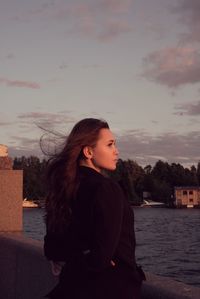 Young woman looking away against sky during sunset