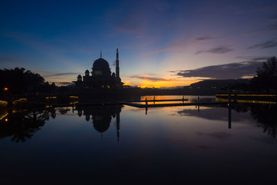 Silhouette putra mosque by lake against sky during sunrise