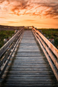 Boardwalk leading towards sea against sky during sunset