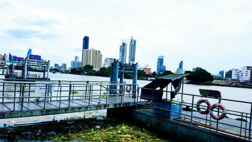 Bridge over river by buildings in city against sky