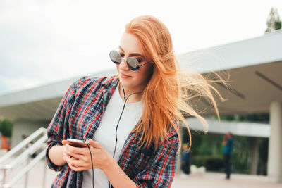 Young woman wearing sunglasses while listening to music in city