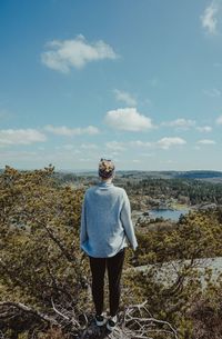 Rear view of woman standing on tree against sky