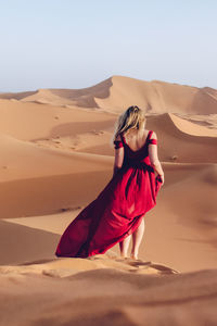 Woman standing on sand dune in desert against clear sky