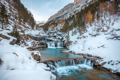 Waterfall amidst snowcapped mountain against sky