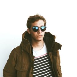 Handsome young man wearing sunglasses and jacket standing against white background