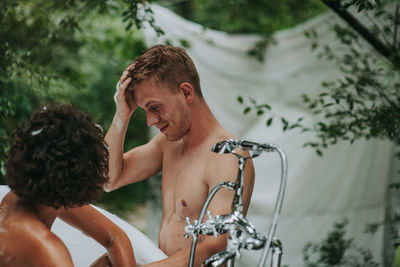 Portrait of shirtless man standing against trees