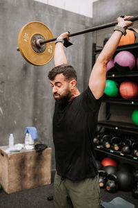 Side view of muscular male athlete doing clean and jerk exercise while training in modern fitness center