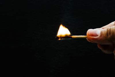 Cropped image of person holding burning matchstick against black background