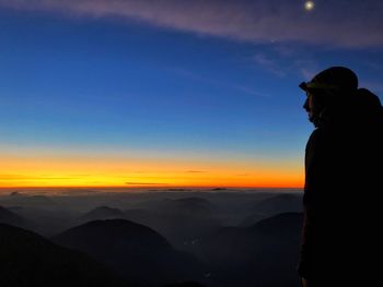 Silhouette man looking at mountains against sky during sunset