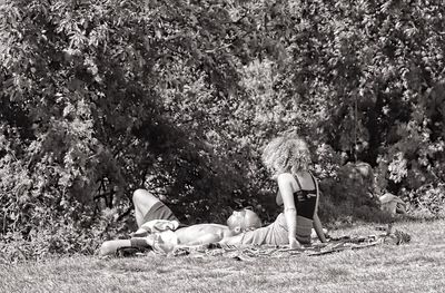 People relaxing on field against trees