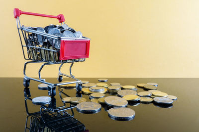 Close-up of coins and shopping cart against yellow background