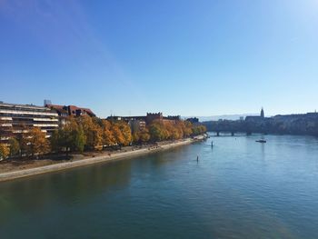 Scenic view of river by buildings against clear blue sky