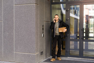 Man ringing intercom with camera near building entrance.