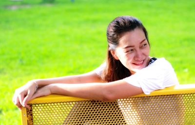 Smiling woman looking away while sitting on bench at park