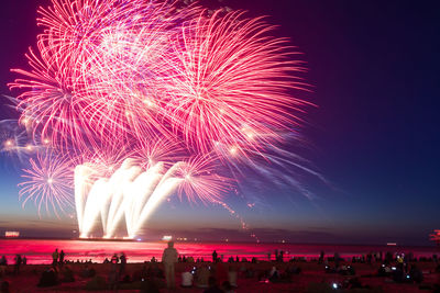 People enjoying firework display at beach during night