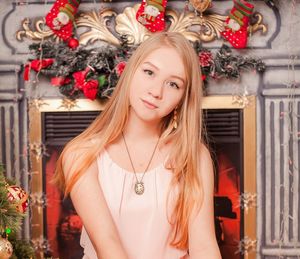 Portrait of beautiful young woman sitting against christmas decoration at home