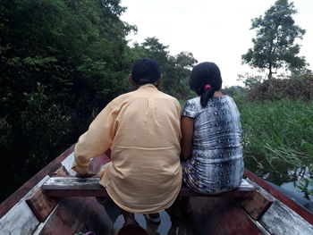 Rear view of friends sitting on plant against trees