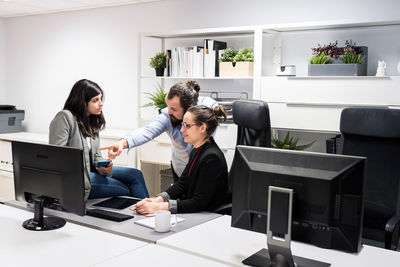 Serious young businessman and female colleagues gathering around computer and discussing business data while working together in contemporary workspace