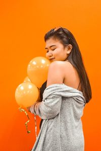 Portrait of young woman standing against orange background