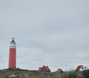 Lighthouse on field by building against sky