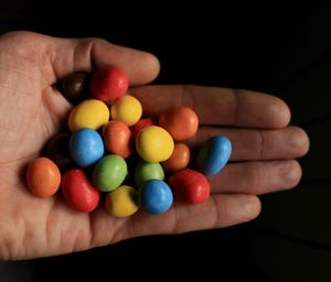 Close-up of hand holding candies against black background
