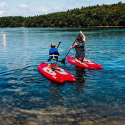 Father and son sitting on lake against sky