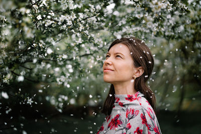 Portrait of a beautiful young woman looking away by blooming tree in spring