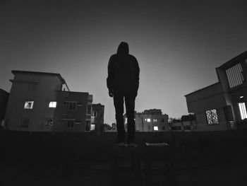 Rear view of silhouette man standing by buildings against sky