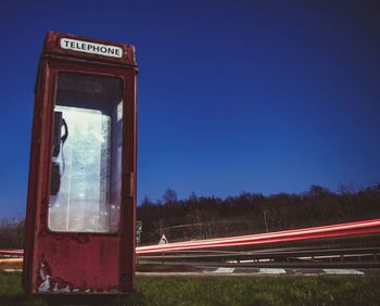 Light trails on road telephone booth by against clear sky at night