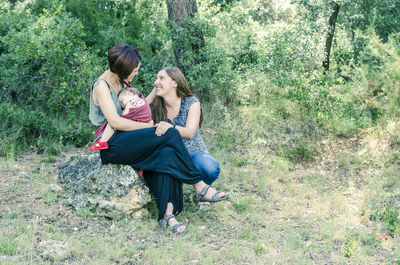 Mother carrying baby with daughter against trees