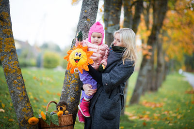 Mother carrying cute baby girl at park during autumn