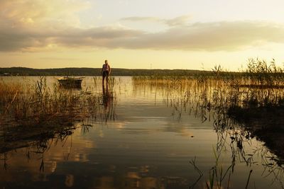 Portrait of woman standing in lake against sky during sunset
